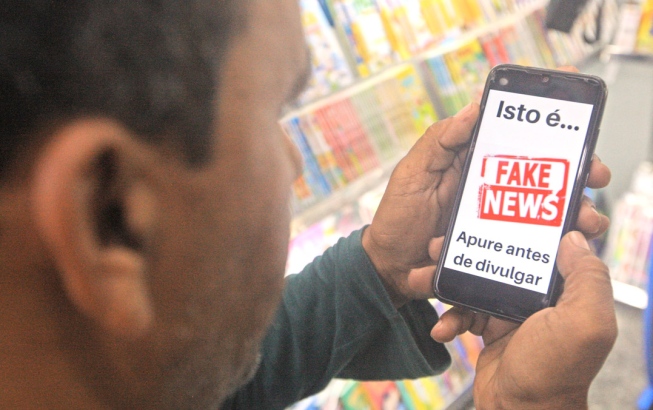 Homem com celular na mão e com a mensagem, isto é Fake news, apure antes de divulgar.